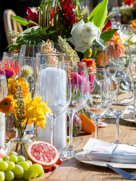Colorful summer BBQ table with tropical flowers, citrus accents, glassware, and outdoor place settings