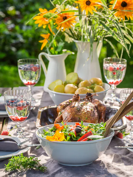 Summer backyard barbecue table with roasted chicken, fresh salad, and yellow Black Eyed Susan floral centerpiece