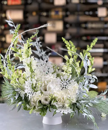 White winter floral arrangement with hydrangea, snapdragons, lisianthus, frosted greens, and snowflake accents – Griffin’s Floral Design