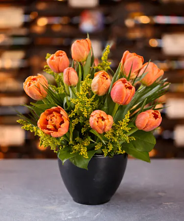 A vibrant bouquet of orange  colorful tulips in a black ceramic bowl. Available for same-day delivery in Columbus, New Albany, and Newark, OH from Griffin’s Floral Design.