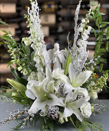 Winter floral design with white lilies, pinecones, frosted branches, and angel figurine Griffins Floral Columbus Ohio